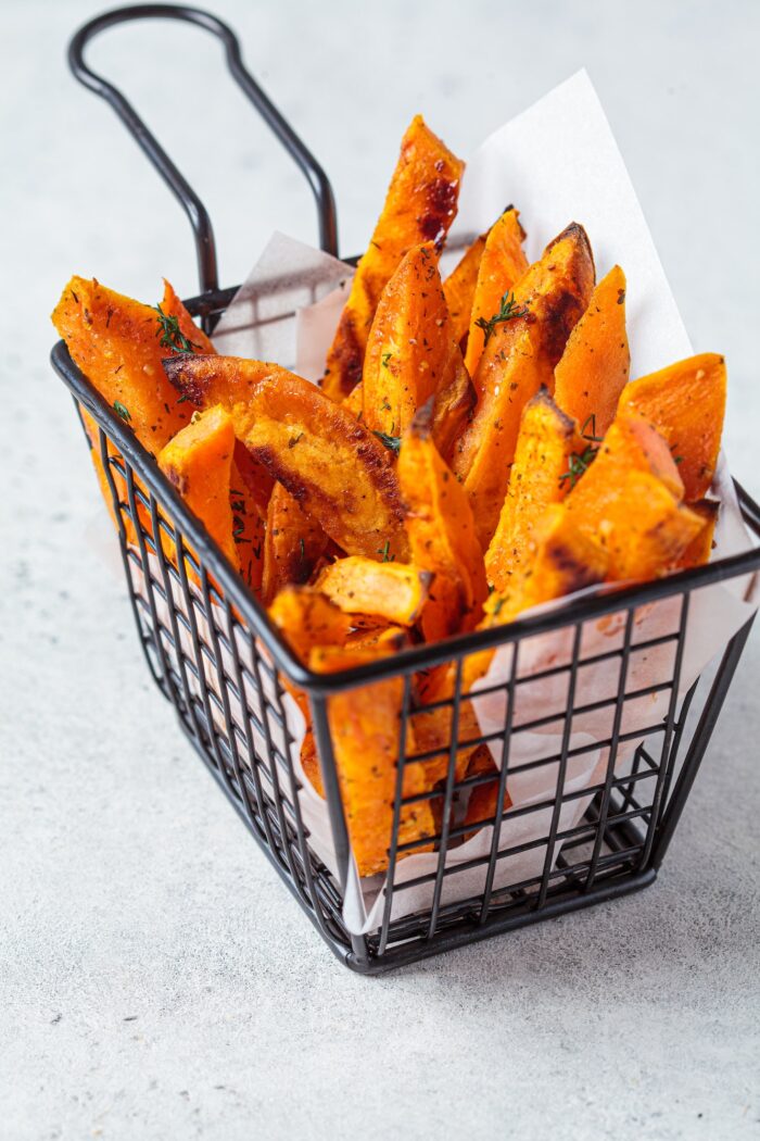 Sweet potato fries in metal basket, gray background. Vegan food concept.